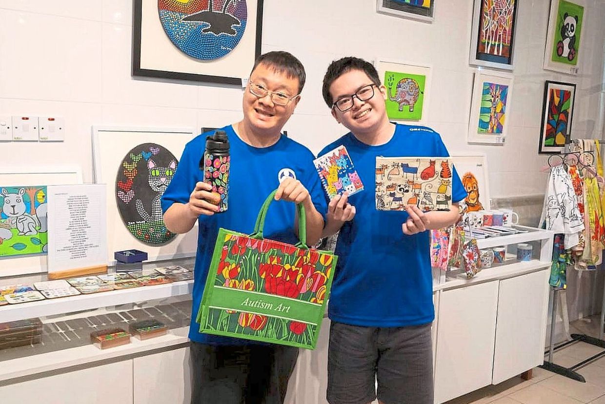 KAA artists displaying Autism Art merchandise including tote bags, notebooks and water bottles